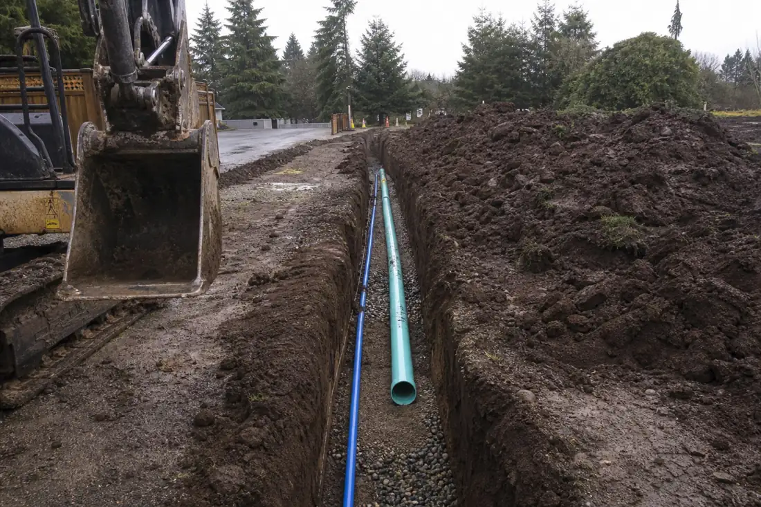 Open utility trench with new water and sewer pipe on gravel bedding in Hillsboro, OR